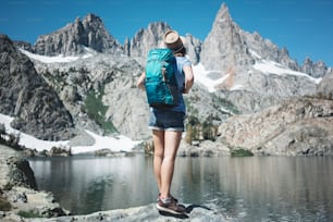 Woman backpacker traveling in the stunning mountain wilderness, standing in front of amazing cold lake