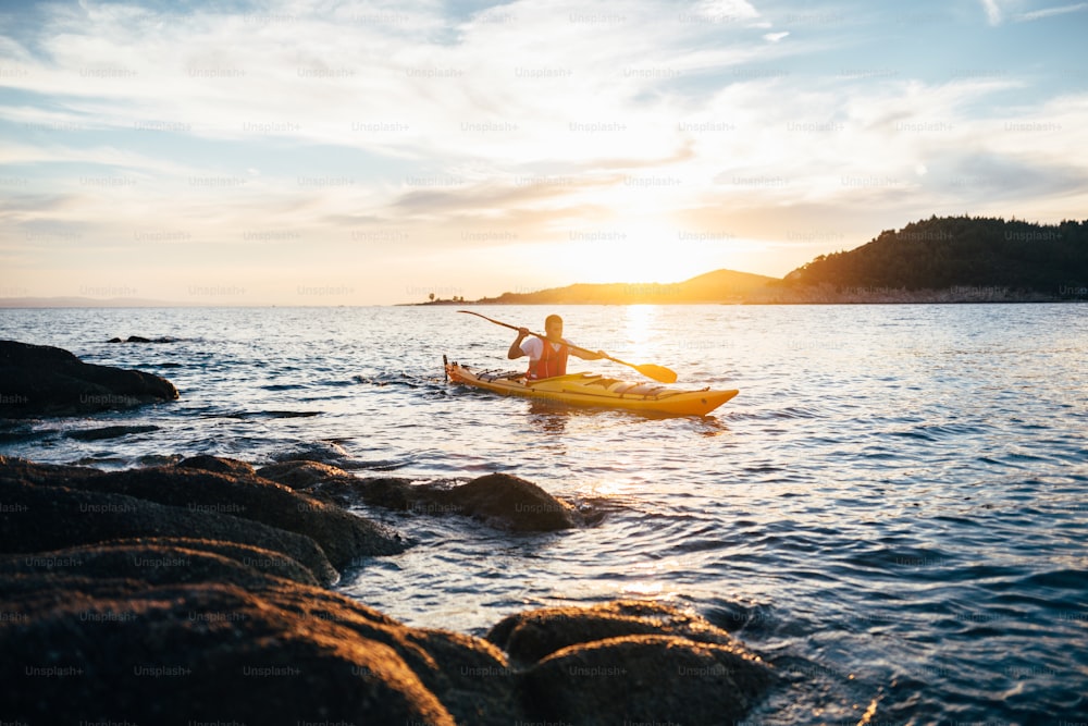 Man kayaker paddling the kayak at sunset sea.
