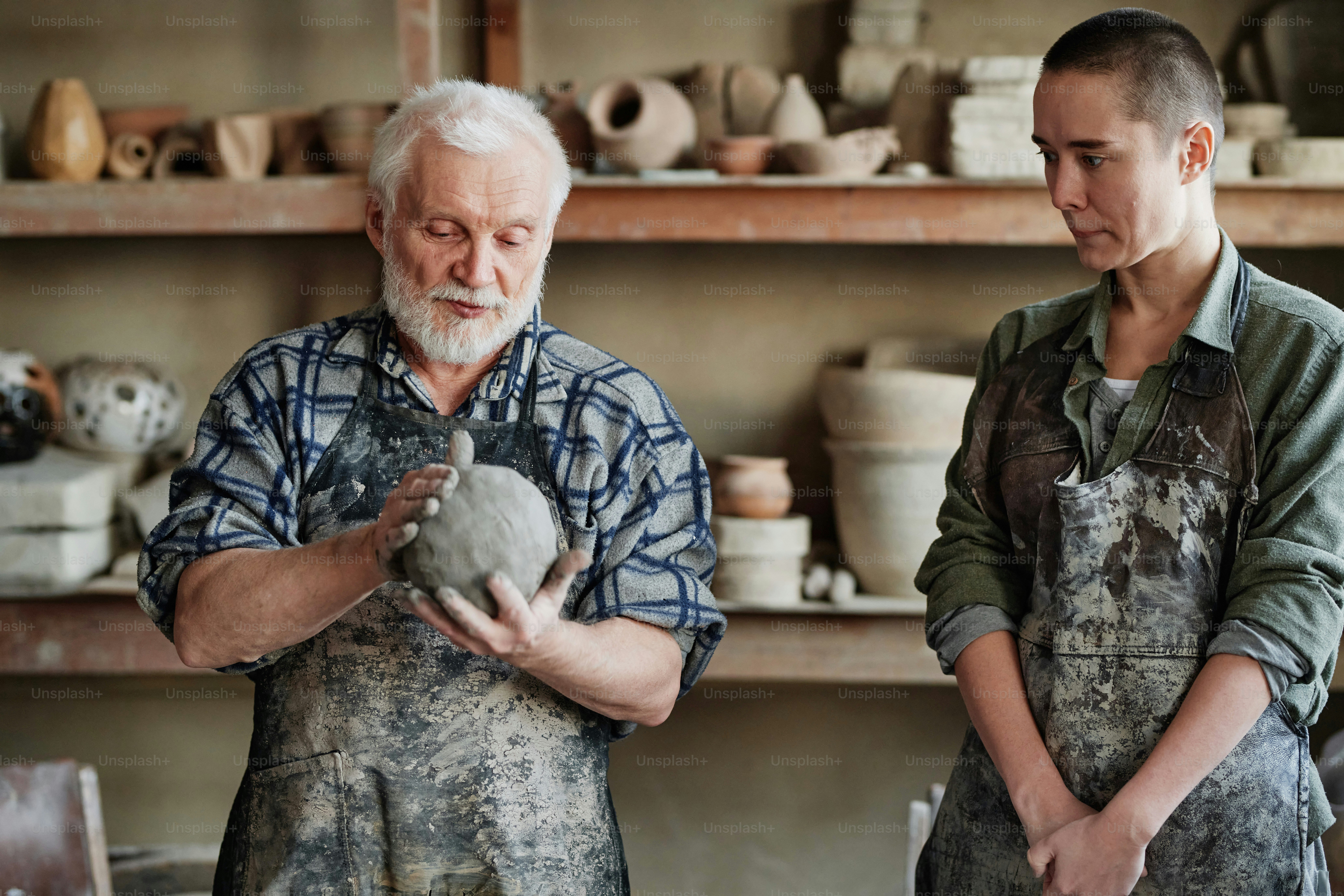Senior man in apron turning a piece of clay in his hands and teaching