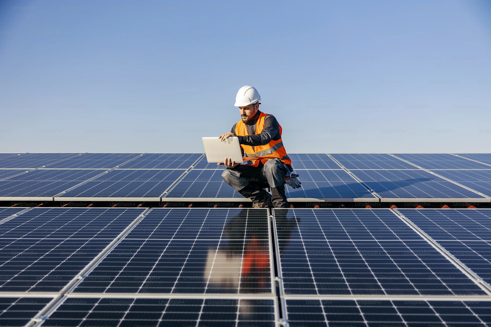 Solar engineer checking system performance on a laptop on a rooftop array