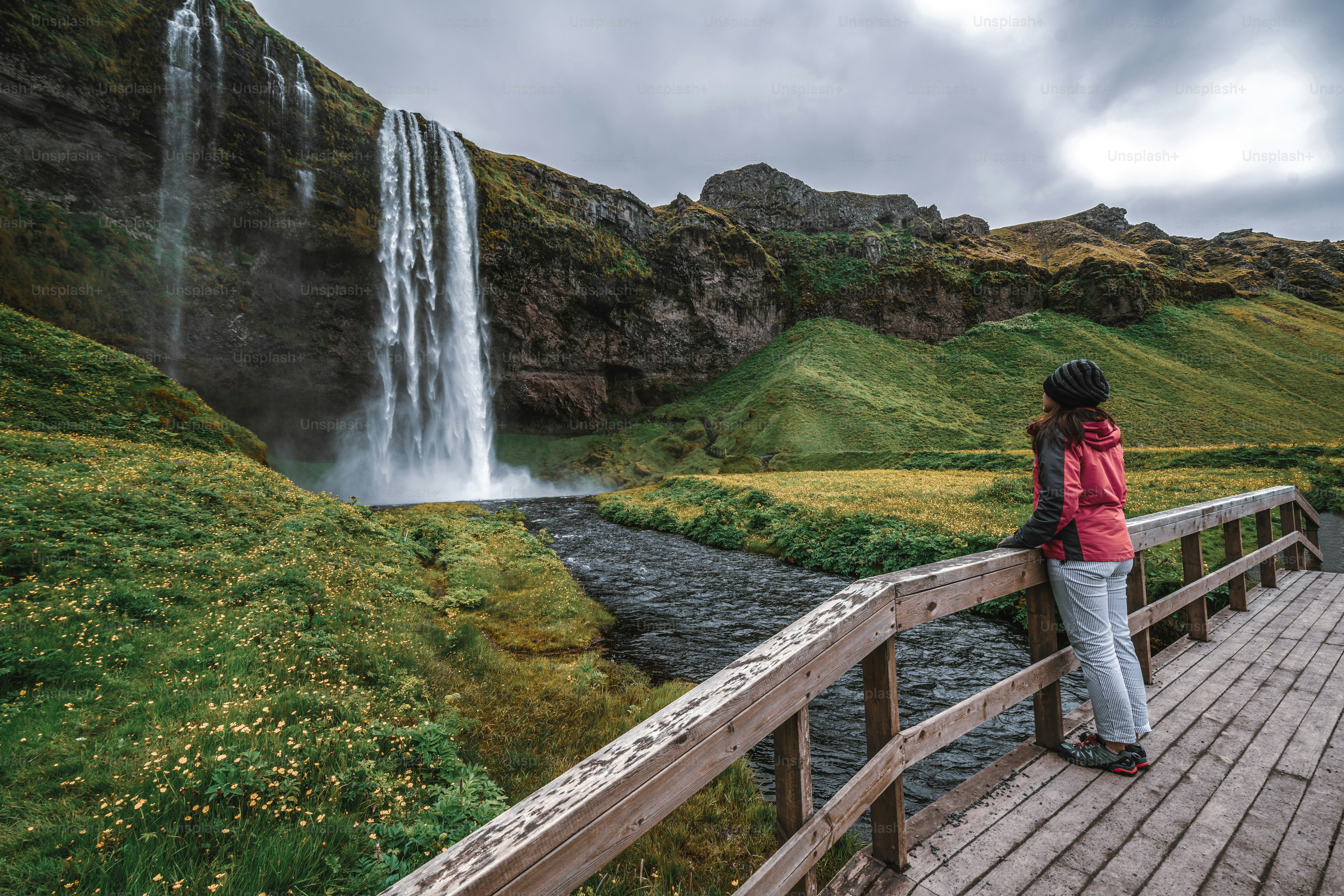 Mulher viajante na cachoeira mágica Seljalandsfoss na Islândia localizada perto do anel viário do sul da Islândia. Majestoso e pitoresco, é um dos lugares de tirar o fôlego mais fotografados do deserto da Islândia