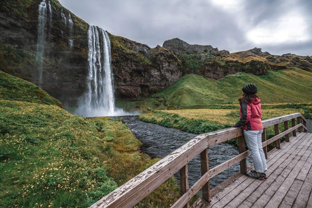 Woman traveler at Magical Seljalandsfoss Waterfall in Iceland located near ring road of South Iceland. Majestic and picturesque, it is one of most photographed breathtaking place of Iceland wilderness