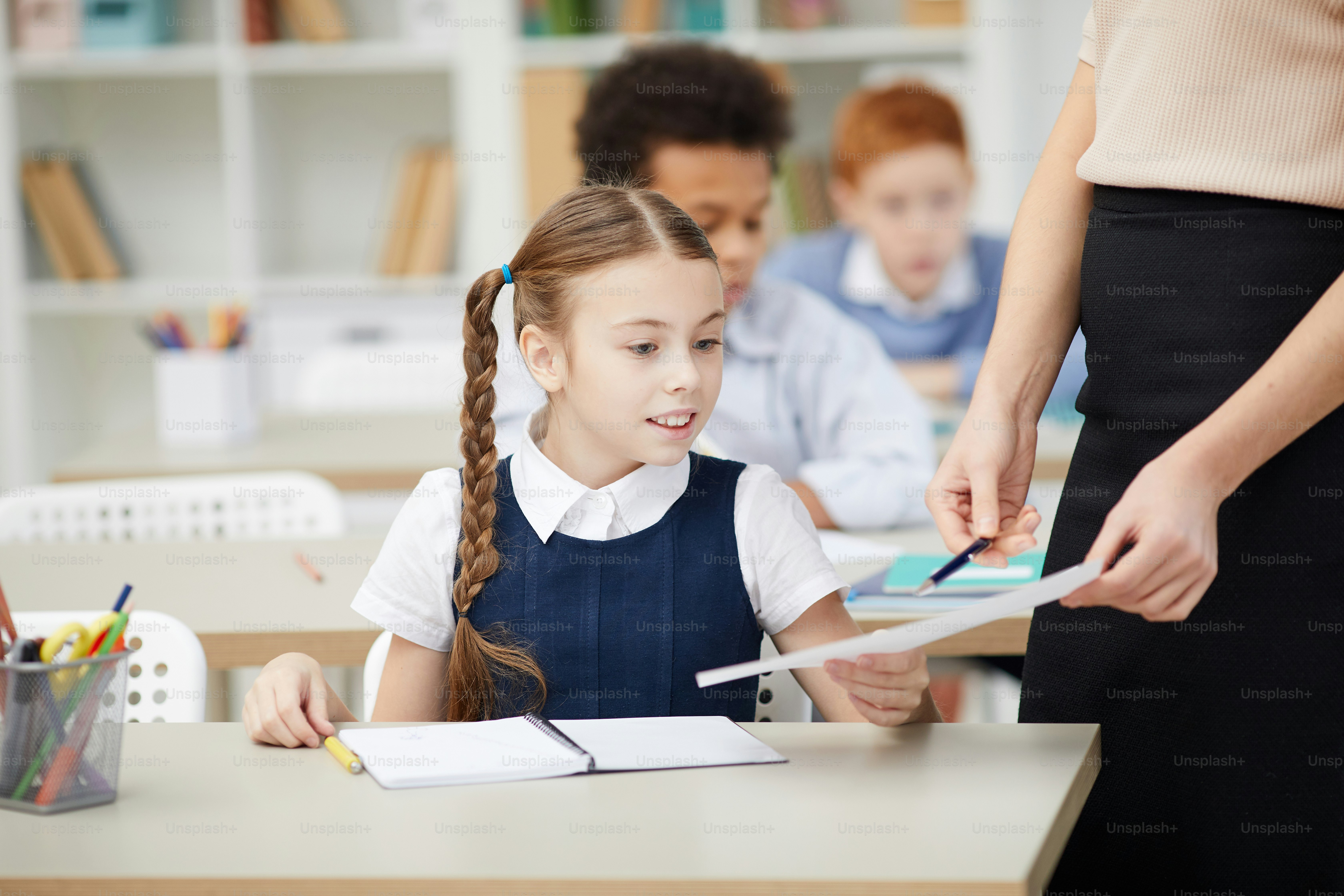 Teacher standing and pointing at paper she showing the work of schoolgirl with good mark during the lesson