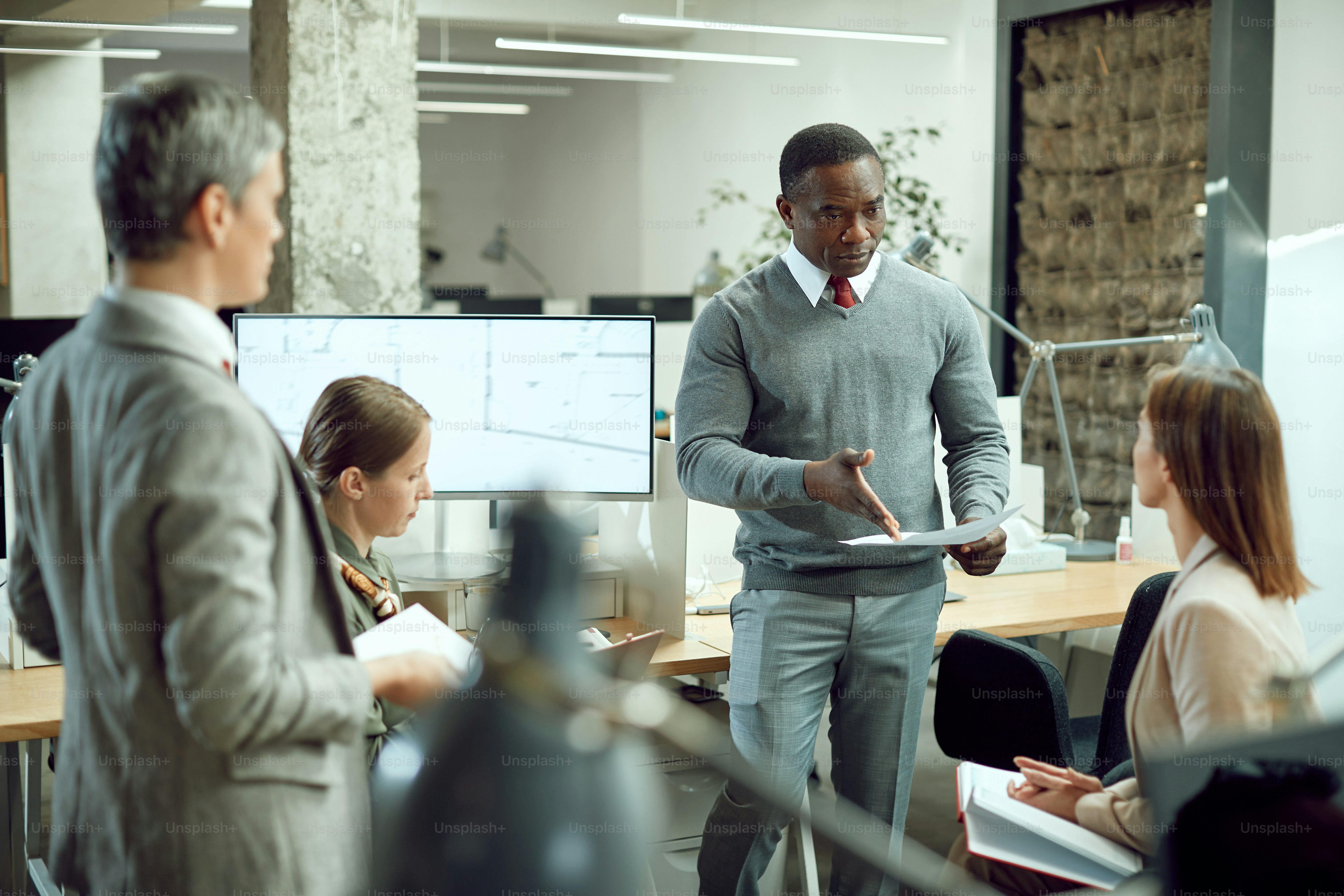 Gerente corporativo afroamericano revisando informes con su equipo de negocios en la oficina.