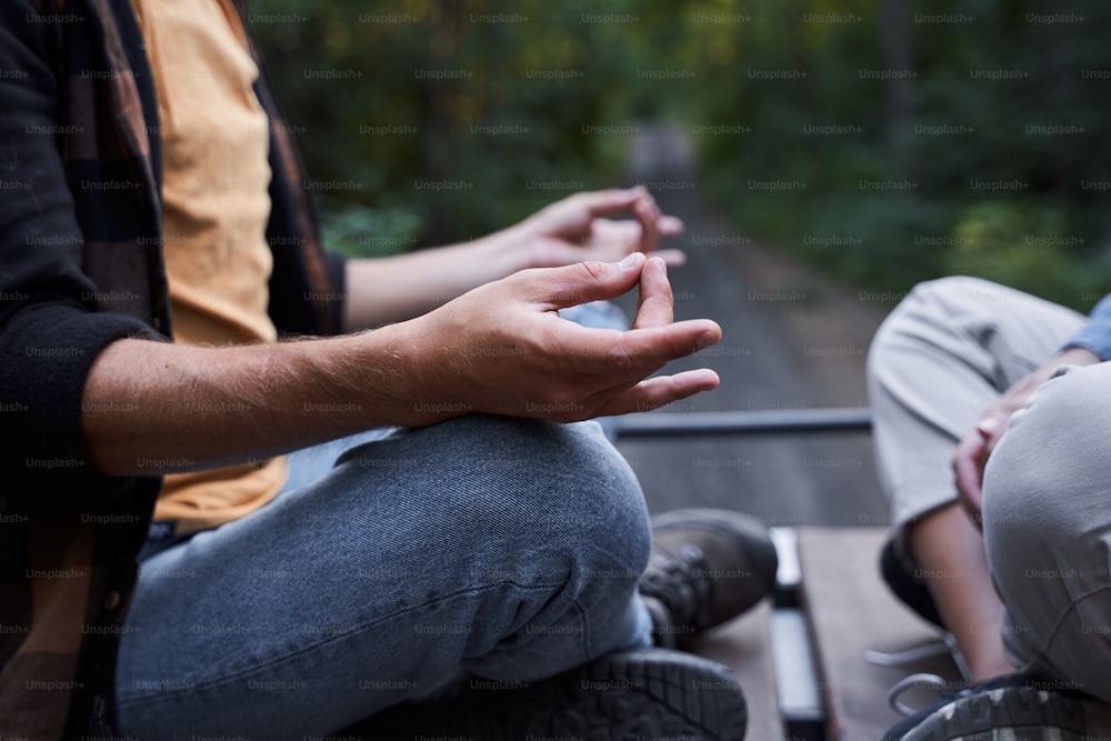 Beschnittenes Foto eines glücklichen jungen Mannes, der der Frau gegenüber sitzt und meditiert, während er sich im Freien ausruht. Konzept von Ruhe und Meditation