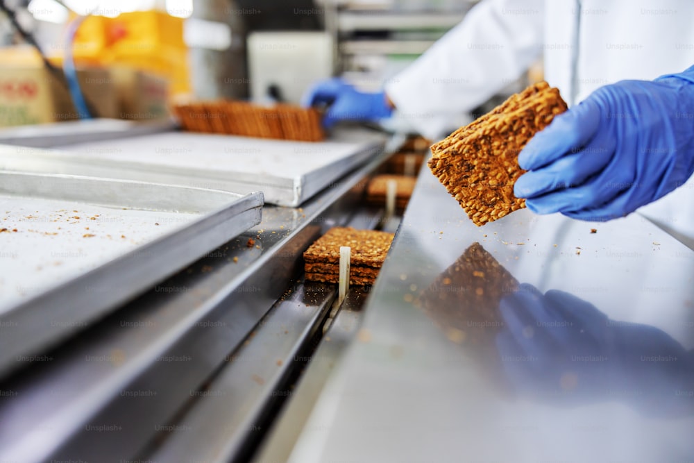 Closeup of worker picking up biscuits form machine while standing in food factory.