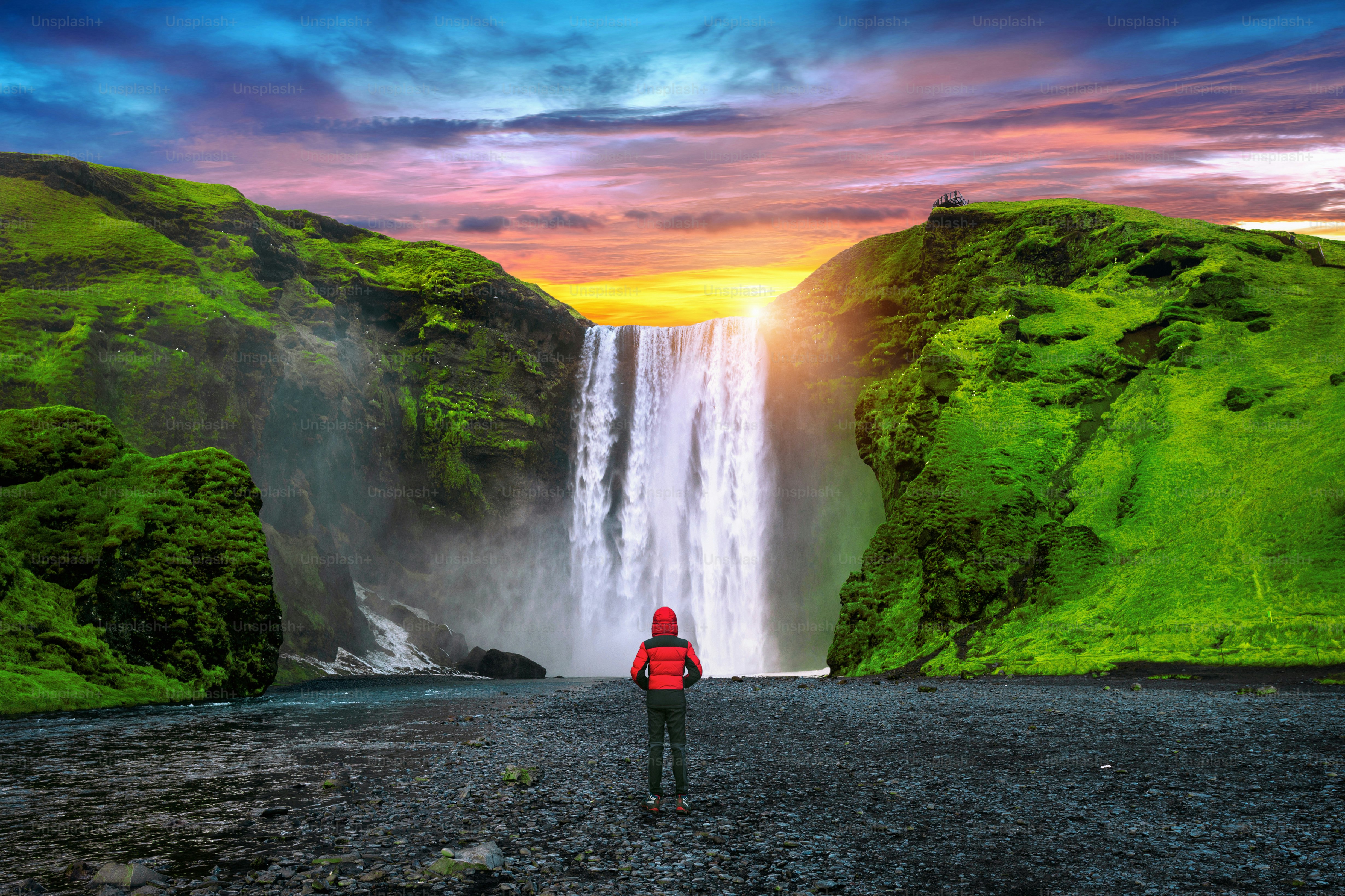 Skogafoss waterfall in Iceland. Guy in red jacket looks at Skogafoss waterfall.