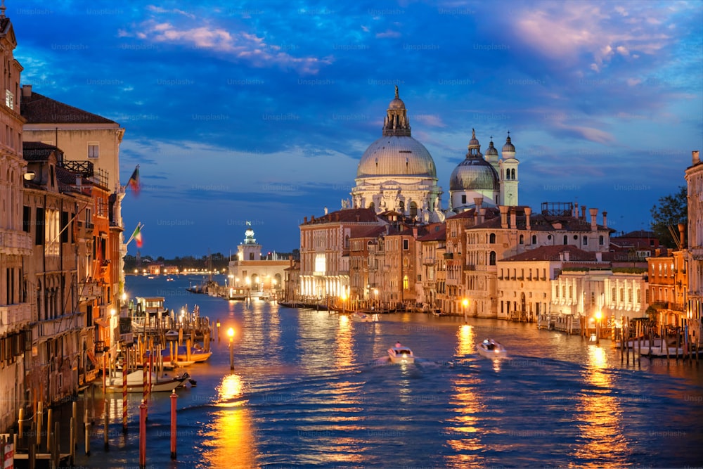 Vista do Grande Canal de Veneza com barcos e da igreja de Santa Maria della Salute à noite da ponte Ponte dell'Accademia. Veneza, Itália