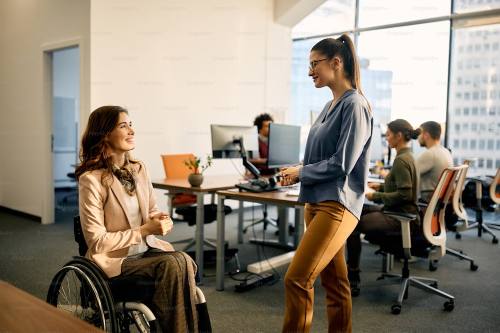 사무실에서 일하는 동안 휠체어를 사용하는 여성 동료와 의사 소통하는 행복한 사업가.
