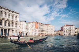 베네치아 곤돌리에가 이탈리아 베니스의 대운하를 통과하는 곤돌라를 펀팅하고 있다. 곤돌라는 바닥이 평평한 전통적인 베네치아 노 젓는 보트입니다. 이탈리아 베니스의 독특한 교통 수단입니다.