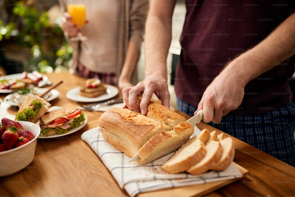 Close-up do homem cortando pão durante o café da manhã em casa.