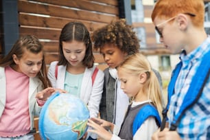 다민족 학교 아이들의 그룹은 자신의 나라의 지리를 배우는 지구를 가리키고 있습니다.