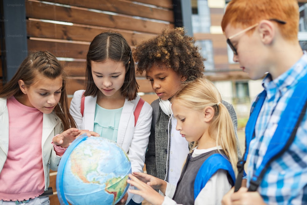 Grupo de escolares multiétnicos señalando el globo terráqueo que aprenden la geografía de su país