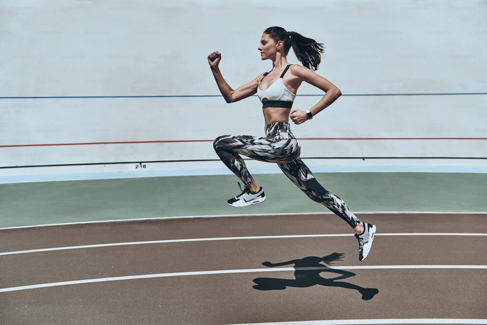 Lunghezza intera di giovane donna in abbigliamento sportivo che corre mentre si esercita all'aperto