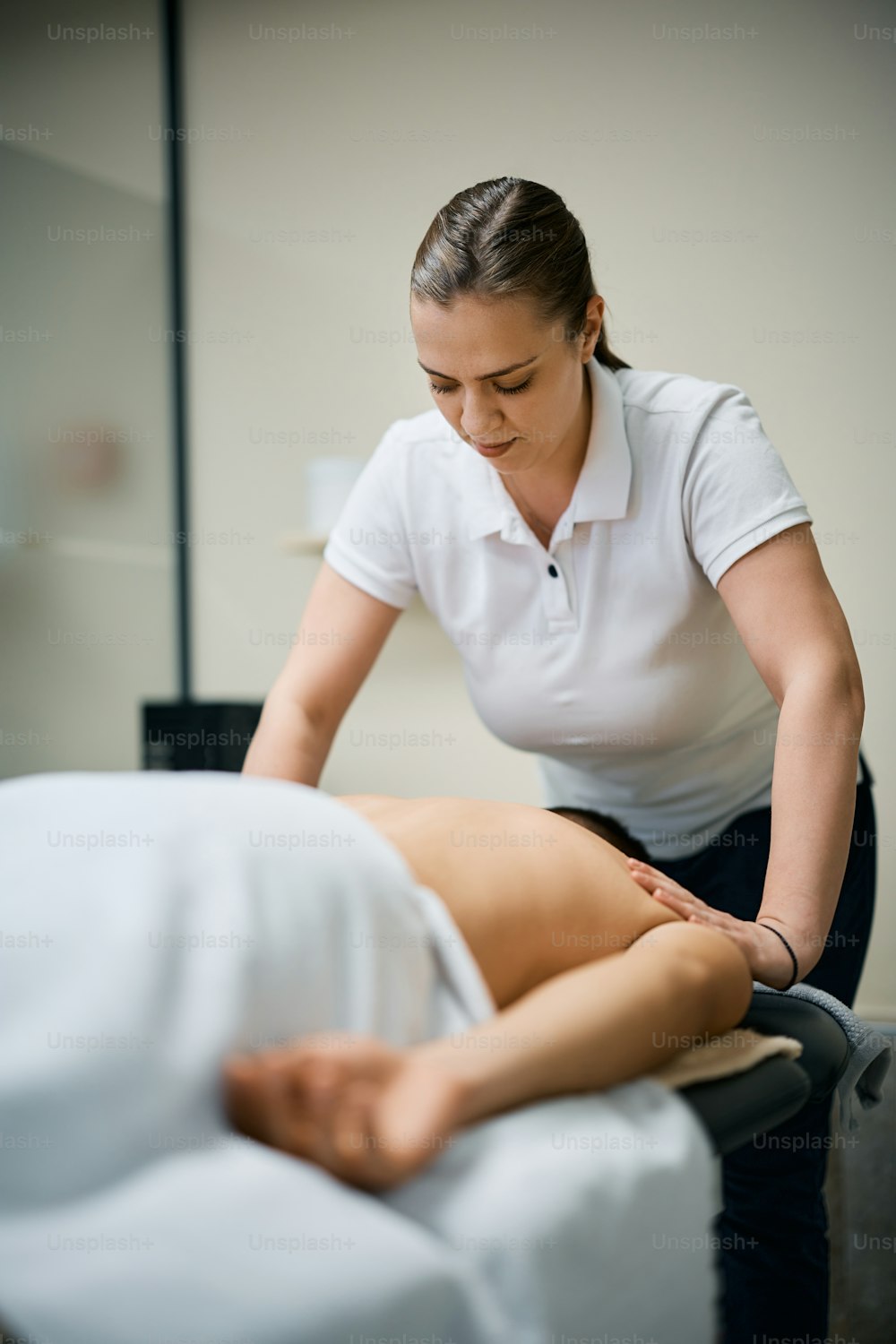 Fisioterapista femminile che massaggia la schiena di un uomo durante il trattamento presso un centro di terapia fisica.