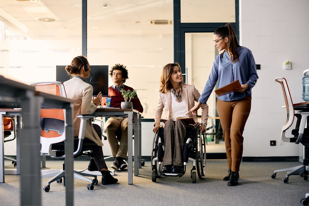 젊은 사업가와 그녀의 여성 동료는 회사 사무실에서 일하는 동안 휠체어 계획을 세웁니다.