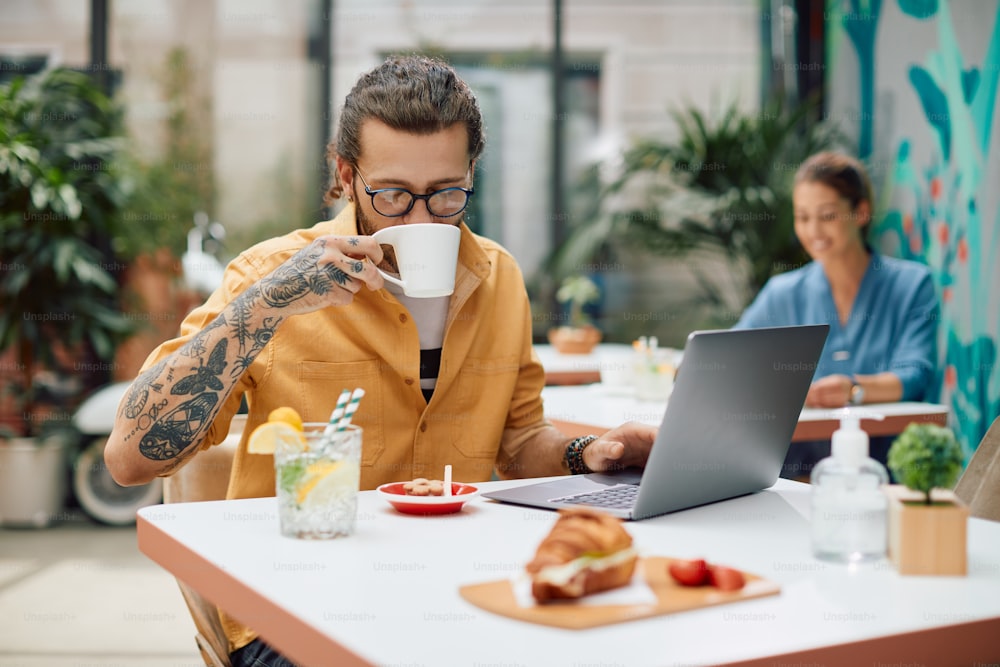 Giovane lavoratore freelance che ha una tazza di caffè mentre lavora su un computer in un bar.