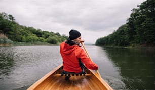 Rear view of man paddling canoe on the lake. Rainy day boat ride.