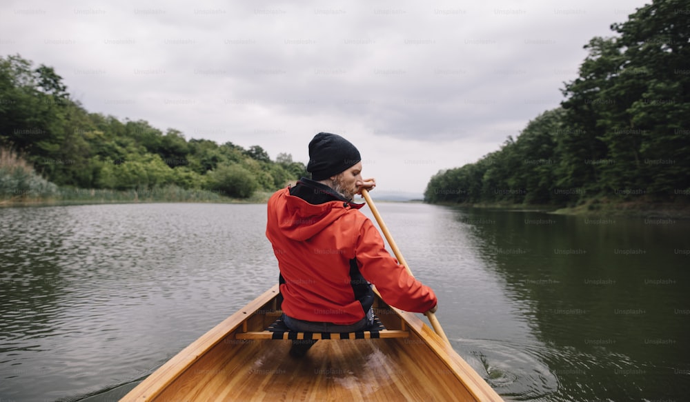 Rear view of man paddling canoe on the lake. Rainy day boat ride.