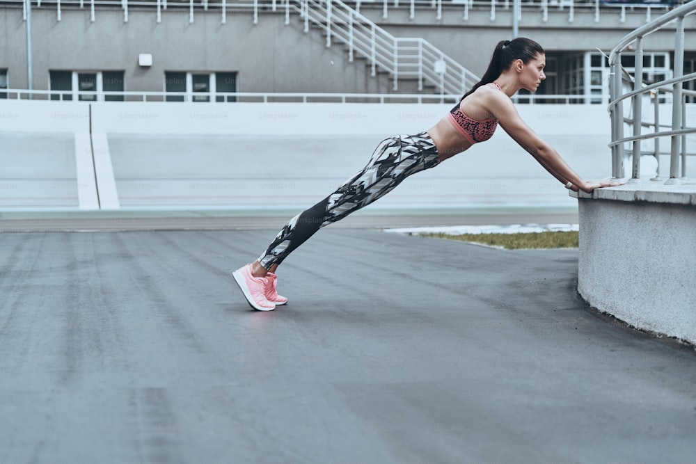 Schöne junge Frau in Sportkleidung, die die Plankenposition hält, während sie im Freien trainiert
