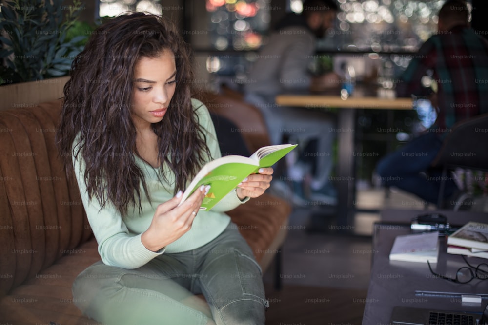 Reading sets me free from boredom. Young student girl at cafe reading book.