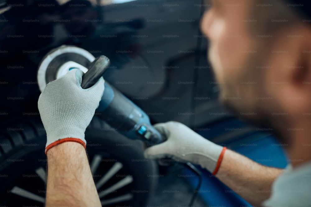 Close-up of worker polishing car at auto service workshop.