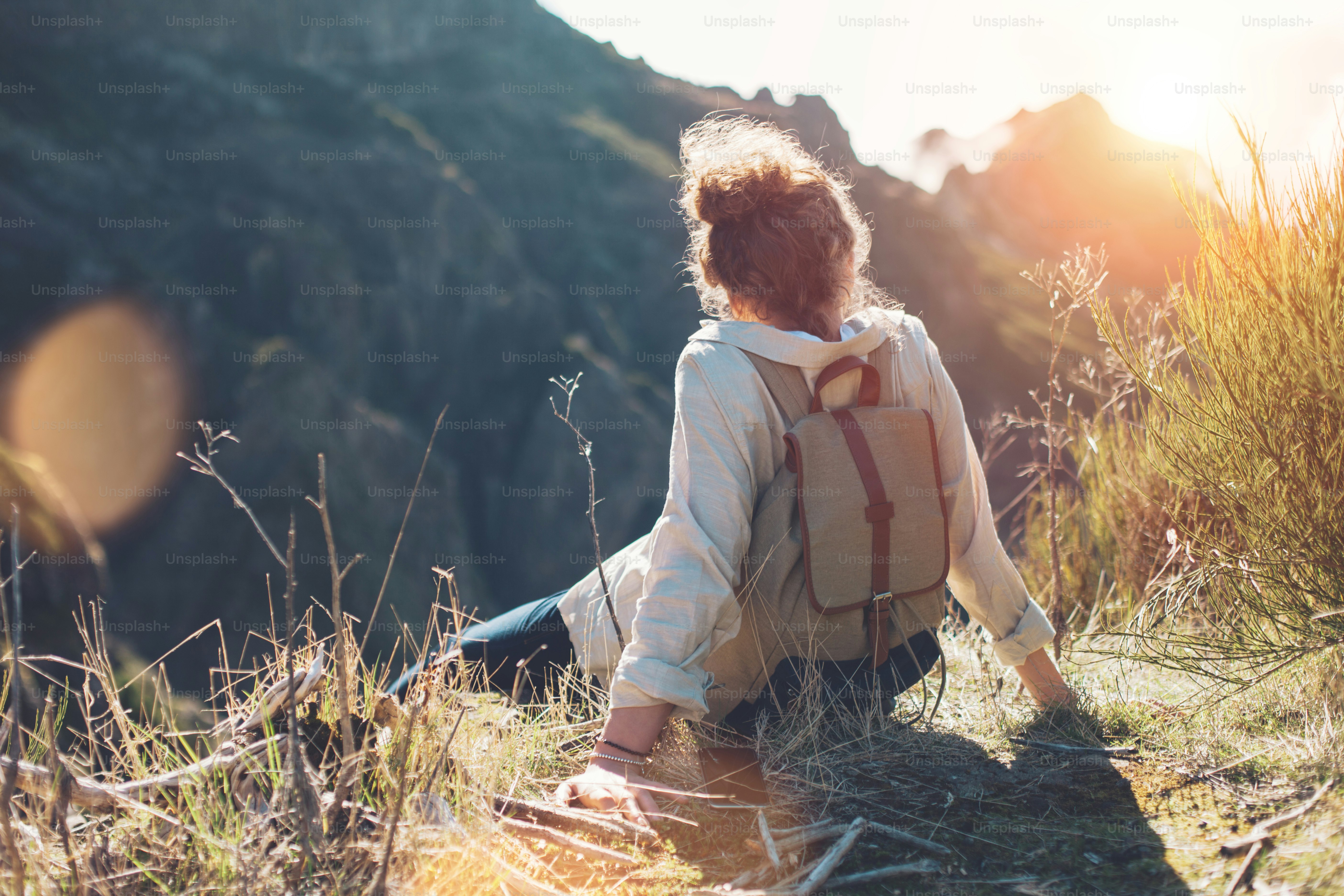 Young woman with backpack sitting on a cliff and enjoying the view of ...