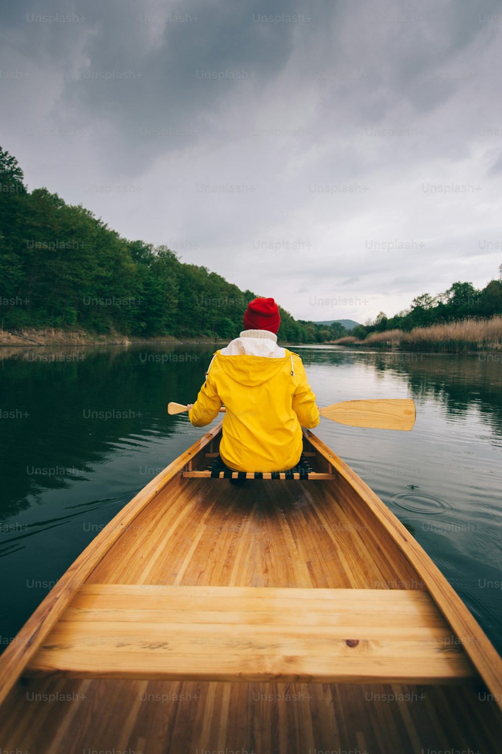 Rear view of woman in yellow raincoat paddling canoe. Enjoy canoeing.