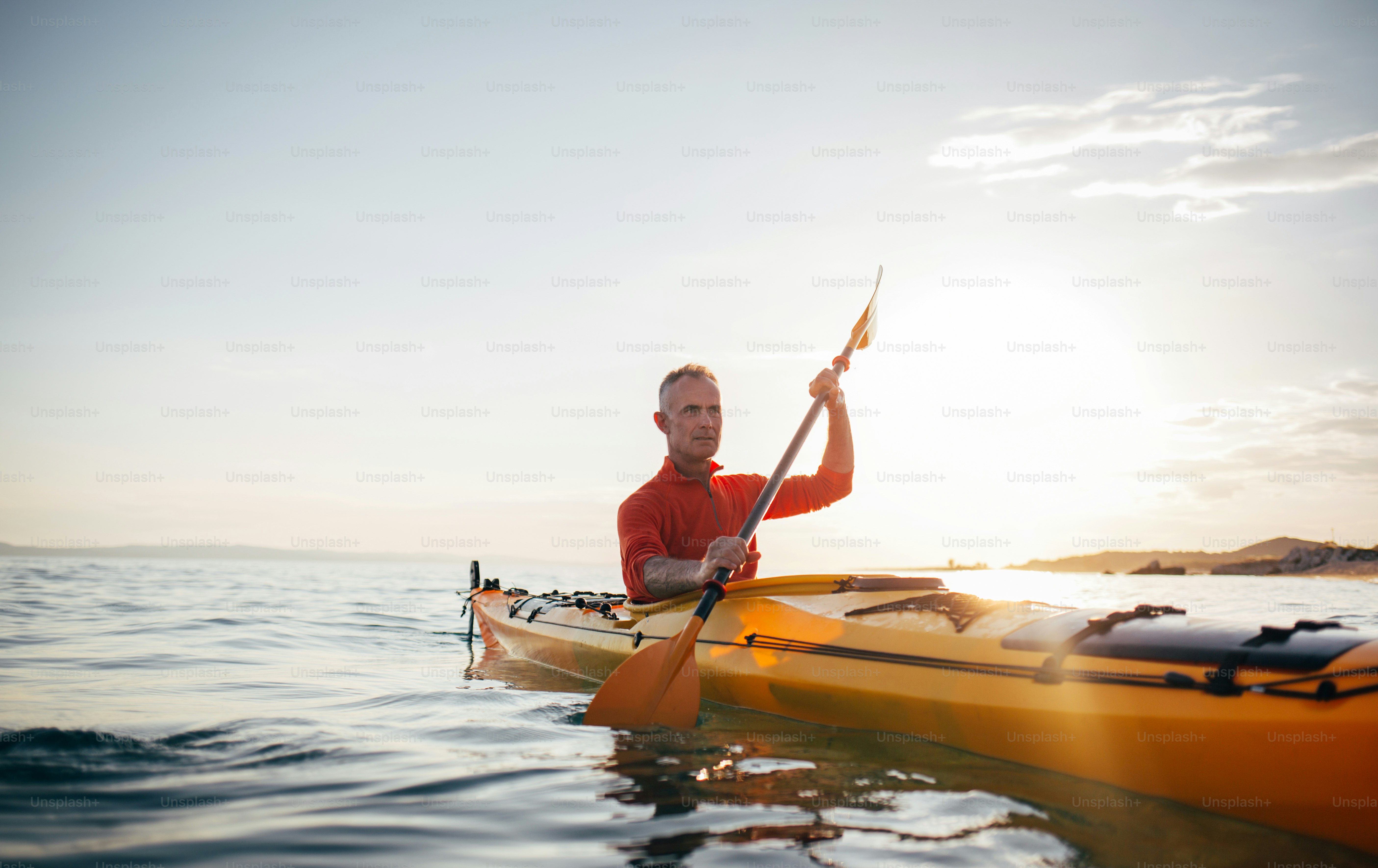 Homme âgé actif pagayant kayak de randonnée sur la mer au coucher du soleil.