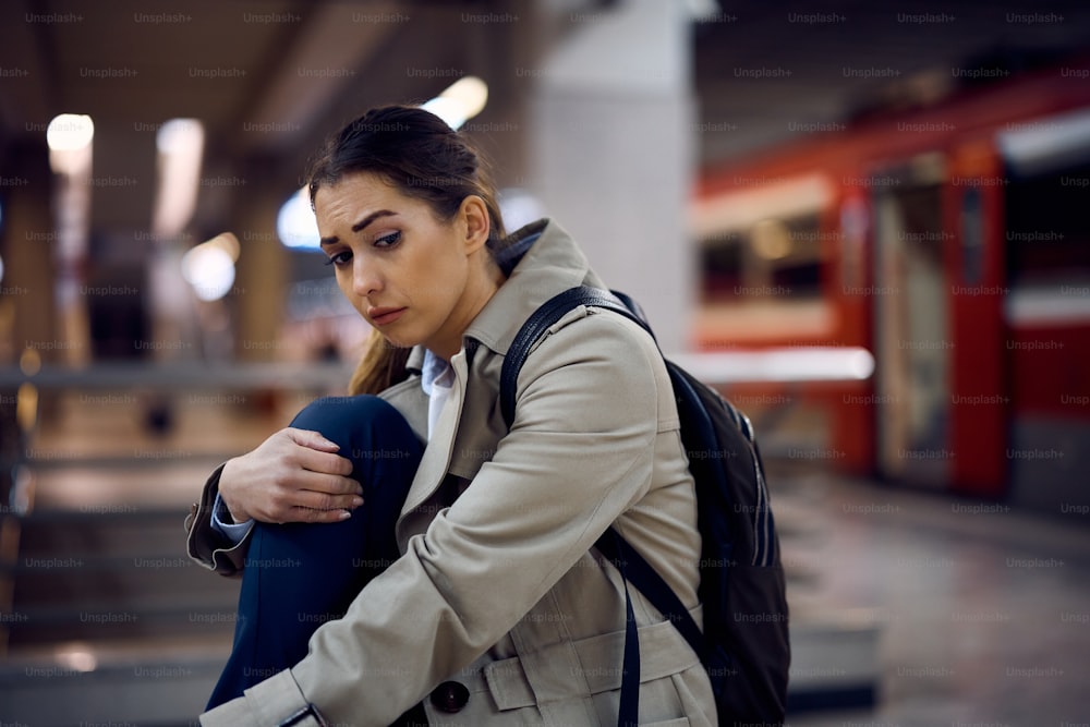 Junge traurige Frau, die an etwas denkt, während sie an der U-Bahn-Station sitzt.