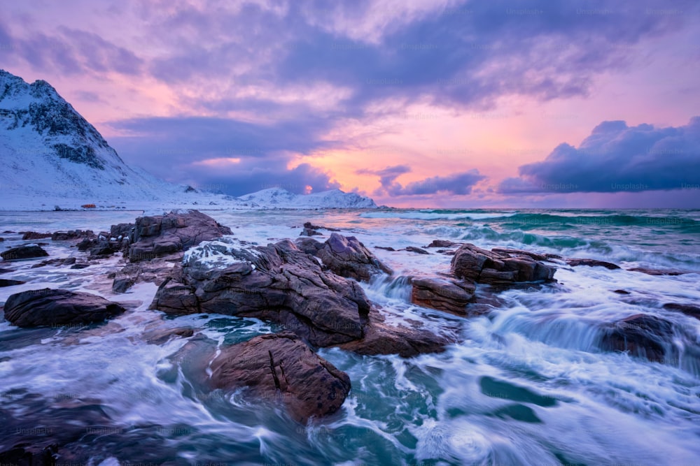 Waves of Norwegian sea on rocky coast in fjord on sunset. Skagsanden beach, Lofoten islands, Norway