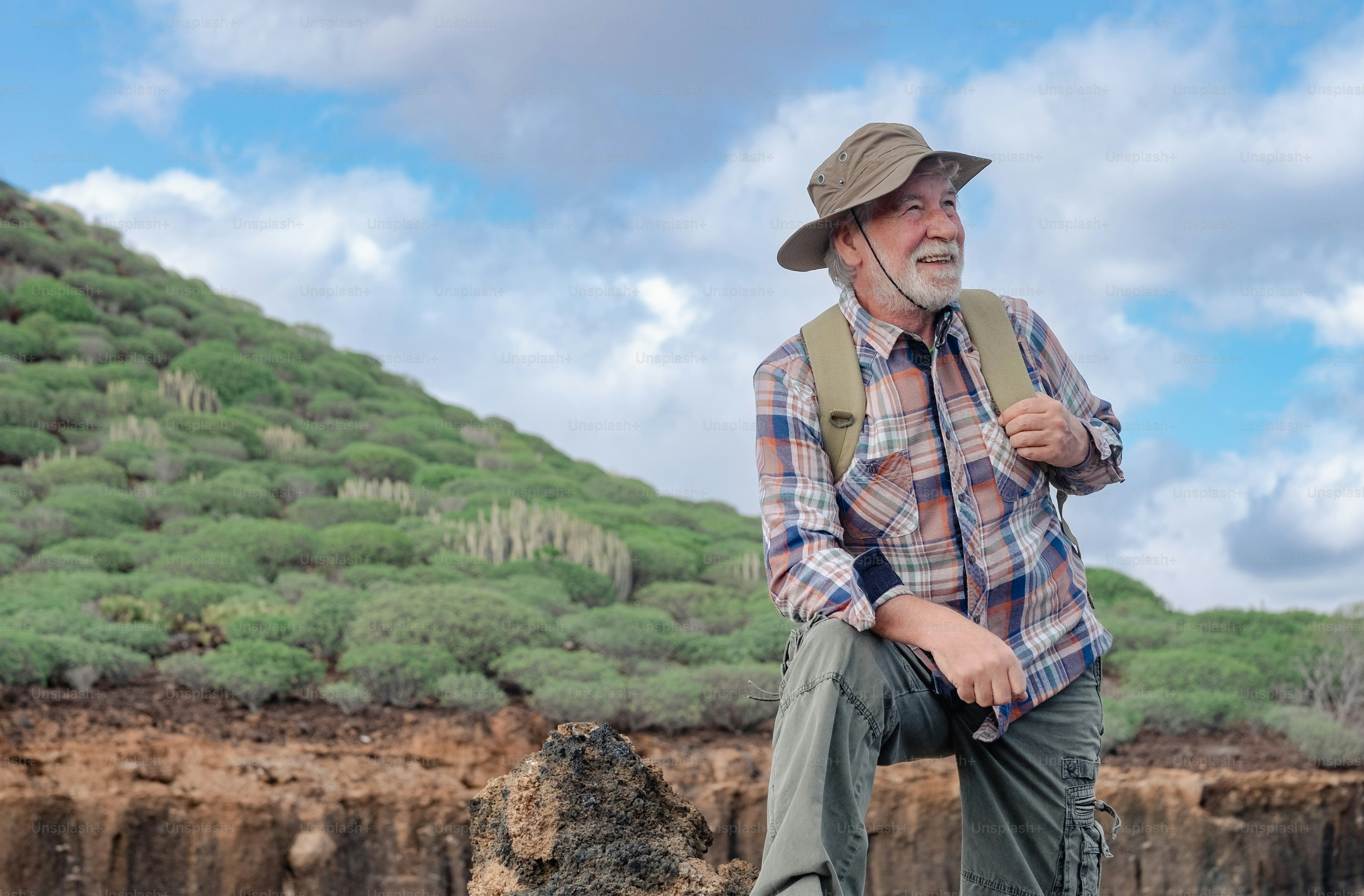 Portrait of a senior bearded man carrying a backpack looking at the mountain and smiling. Fit old man on a hiking trip enjoying adventure freedom and healthy vacation