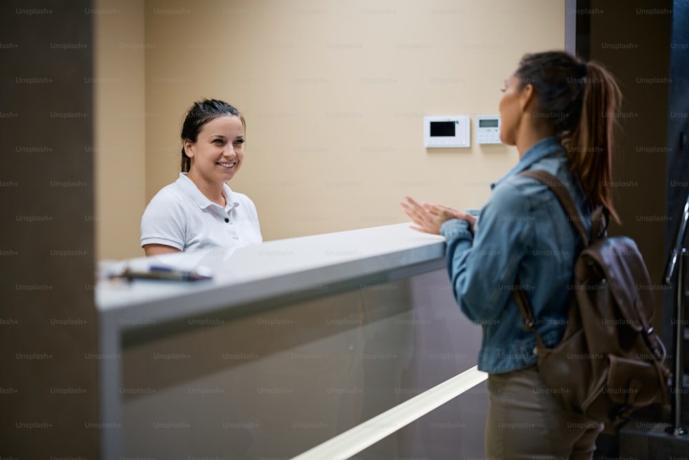 Happy physical therapist communicating with female patient at reception desk at the clinic.