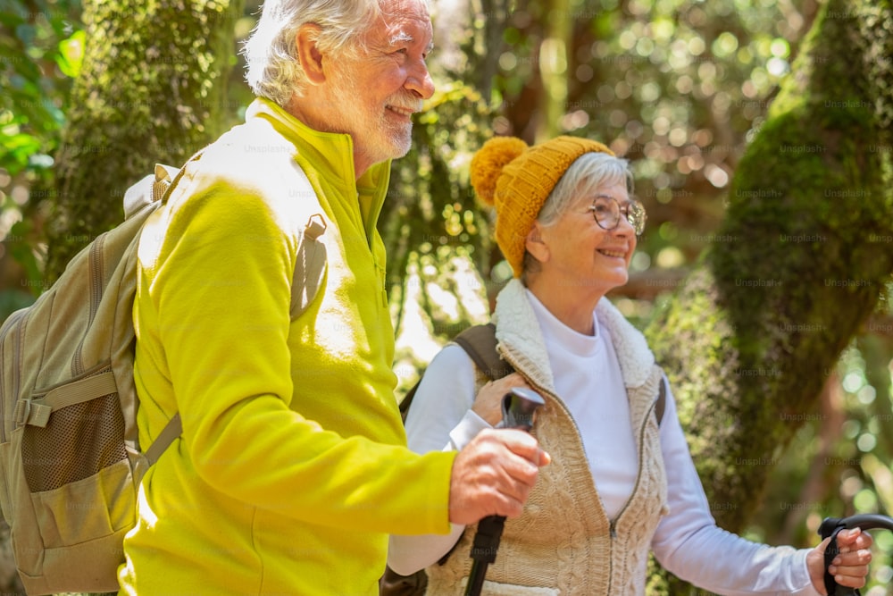 Happy caucasian senior couple with backpack and walking sticks hike in the forest enjoying healthy lifestyle and retirement