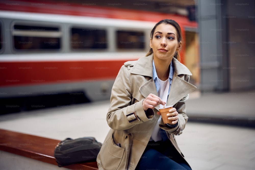 기차역에서 기다리는 동안 테이크아웃 커피를 마시는 젊은 여성.