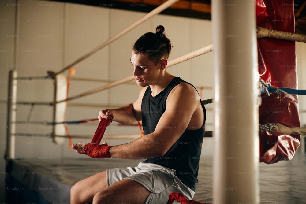 Male boxer getting ready for training and wrapping fists with boxing bandage in a gym.