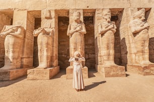 A happy tourist girl in a dress is interested in Egyptology and archaeology and gets a travel experience at the Karnak Temple in Luxor.