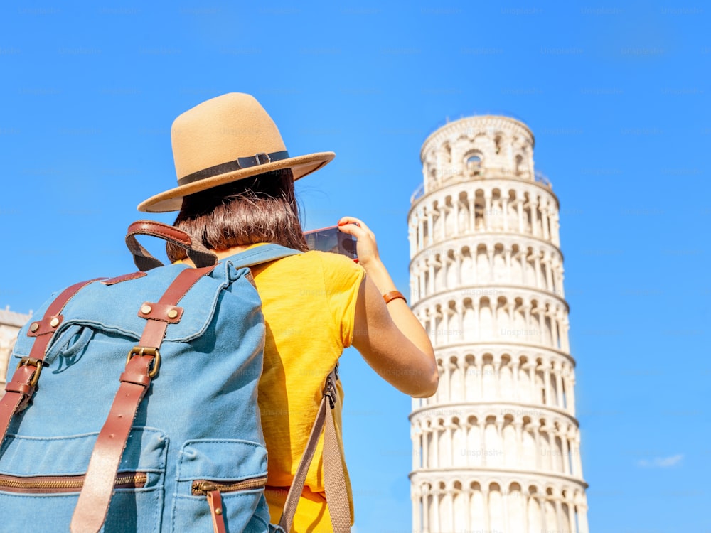 Feliz viajante do sexo feminino no chapéu com mochila tirando foto da torre inclinada em Pisa. Conceito de férias e estilo de vida