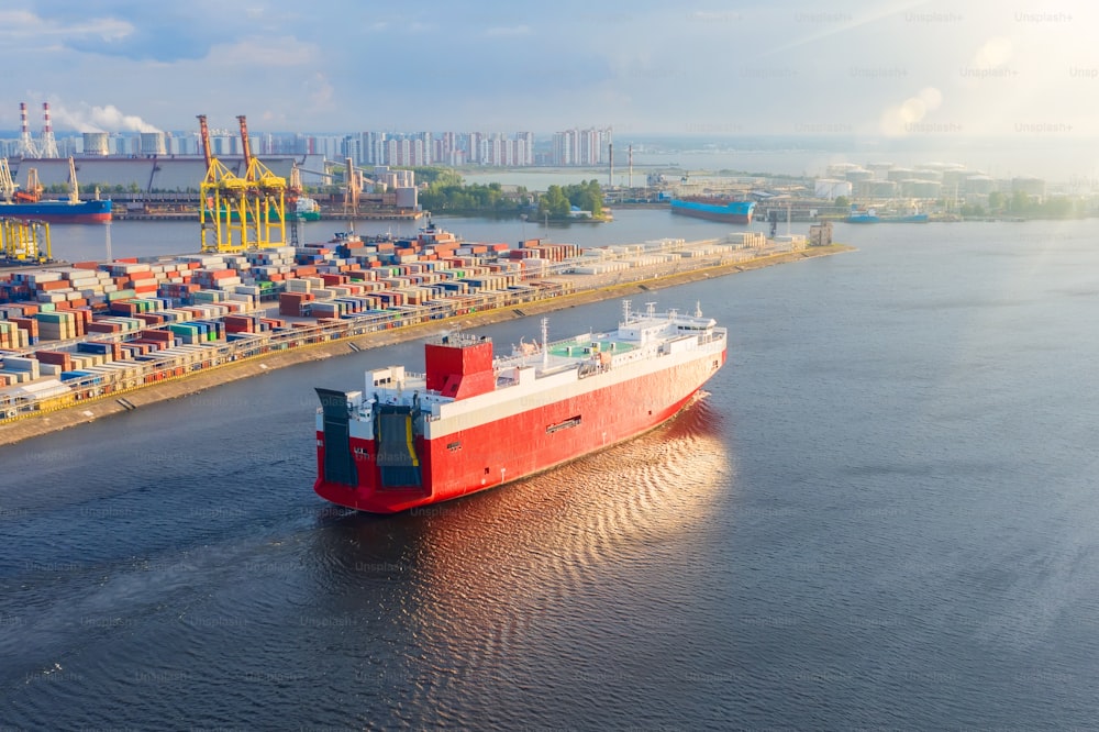 Barco rojo de carga para el transporte de automóviles y otras velas de transporte nuevas desde el puerto hasta el mar, puesta del sol de la tarde