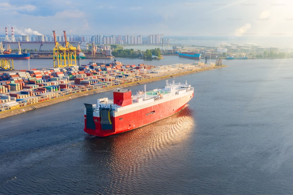 Cargo red ship for the transport of cars and other new transport sails from the port to the sea, evening sunset