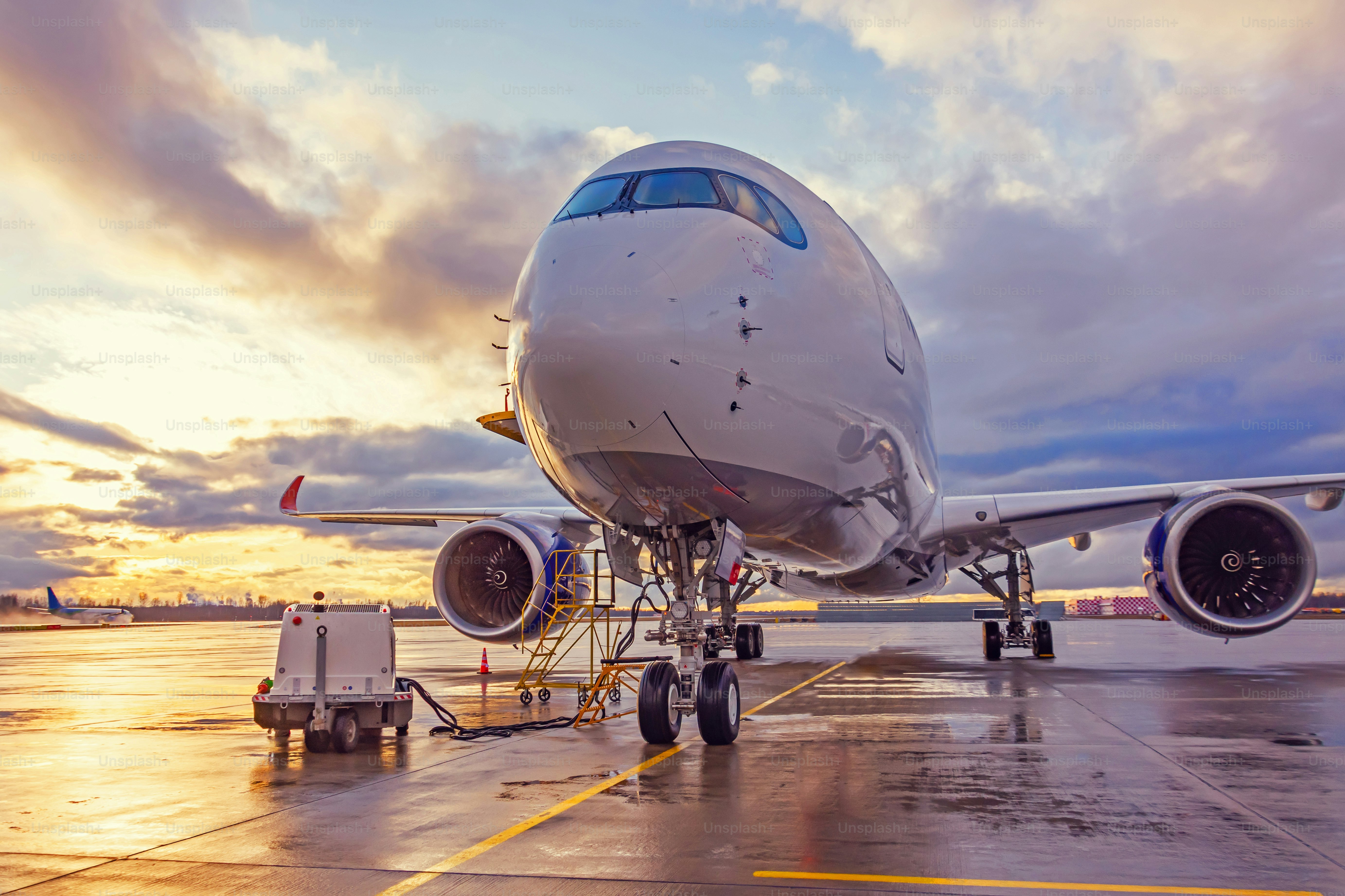 View of an airplane parked at an airport during sunset bright light shine and clouds in the sky