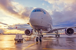 View of an airplane parked at an airport during sunset bright light shine and clouds in the sky