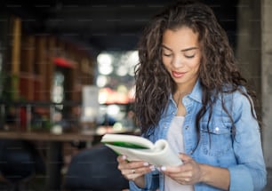 Perdido em cada página. Menina afro-americana no café lendo o livro.