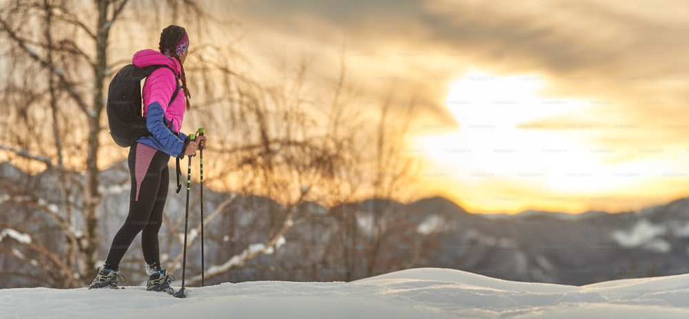 Ein sportliches Mädchen beobachtet den Sonnenuntergang während einer Schneeschuhwanderung