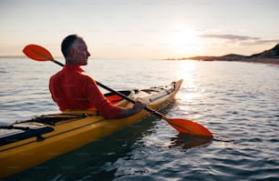 Rear view of active senior man enjoy paddling kayak on the sunset sea.