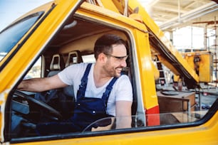 Smiling handsome caucasian worker in overall entering excavator and looking over shoulder.