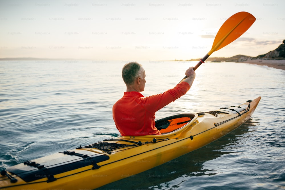 Rear view of active senior man enjoy paddling kayak on the sunset sea.
