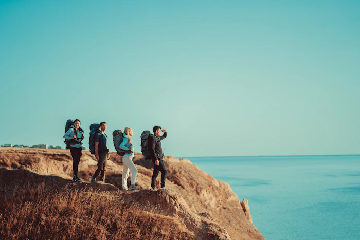 Four travelers with backpacks standing on a clifftop above the sea