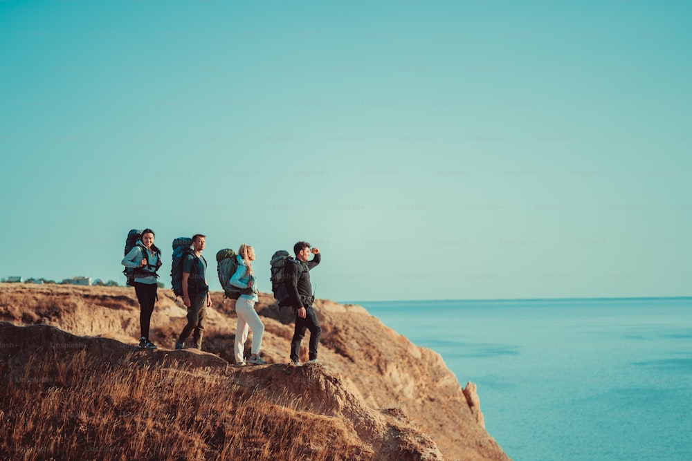 The four travelers with backpacks standing on the mountain top above the sea