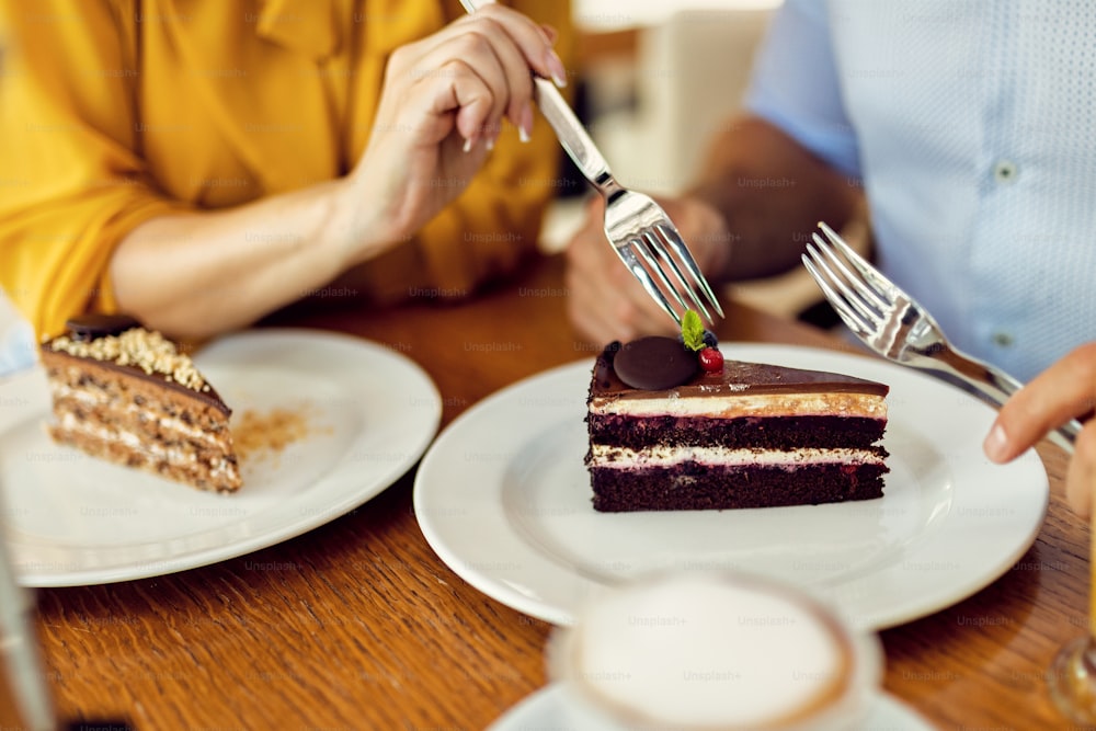 Close-up of of woman tasting boyfriend's cake while having dessert in a cafe.